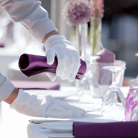 a waiter is putting purple napkins on a table.