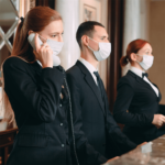 a group of people wearing surgical masks and one female talking on the phone at hotel reception.