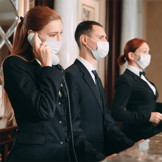 a group of people wearing surgical masks and one female talking on the phone at hotel reception.