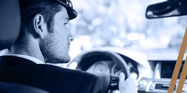 A man in a suit is driving a car, and he is looking towards the right-side mirror.